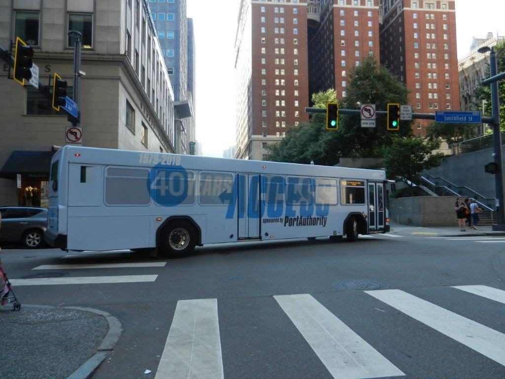 A city bus with ACCESS' 40 Year Anniversary logo wrapped around the entire bus. The bus is turning onto a street.